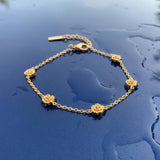 Gold bracelet with five stationary gold rosebud designs spaced out on the chain on a wet blue surface