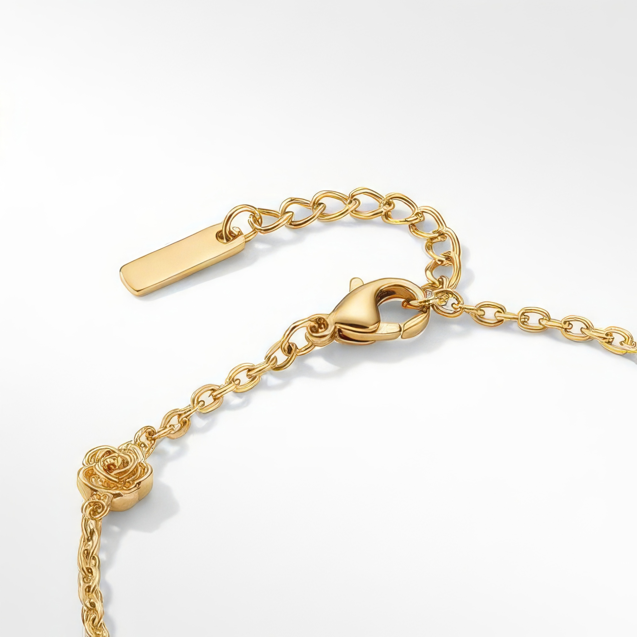 Close up of clasp of gold bracelet with stationary gold rosebud designs spaced out on the chain on a white background