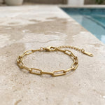 Gold paperclip chain bracelet on a wet stone surface at the edge of a pool