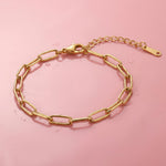 Gold paperclip chain bracelet on a wet pink surface
