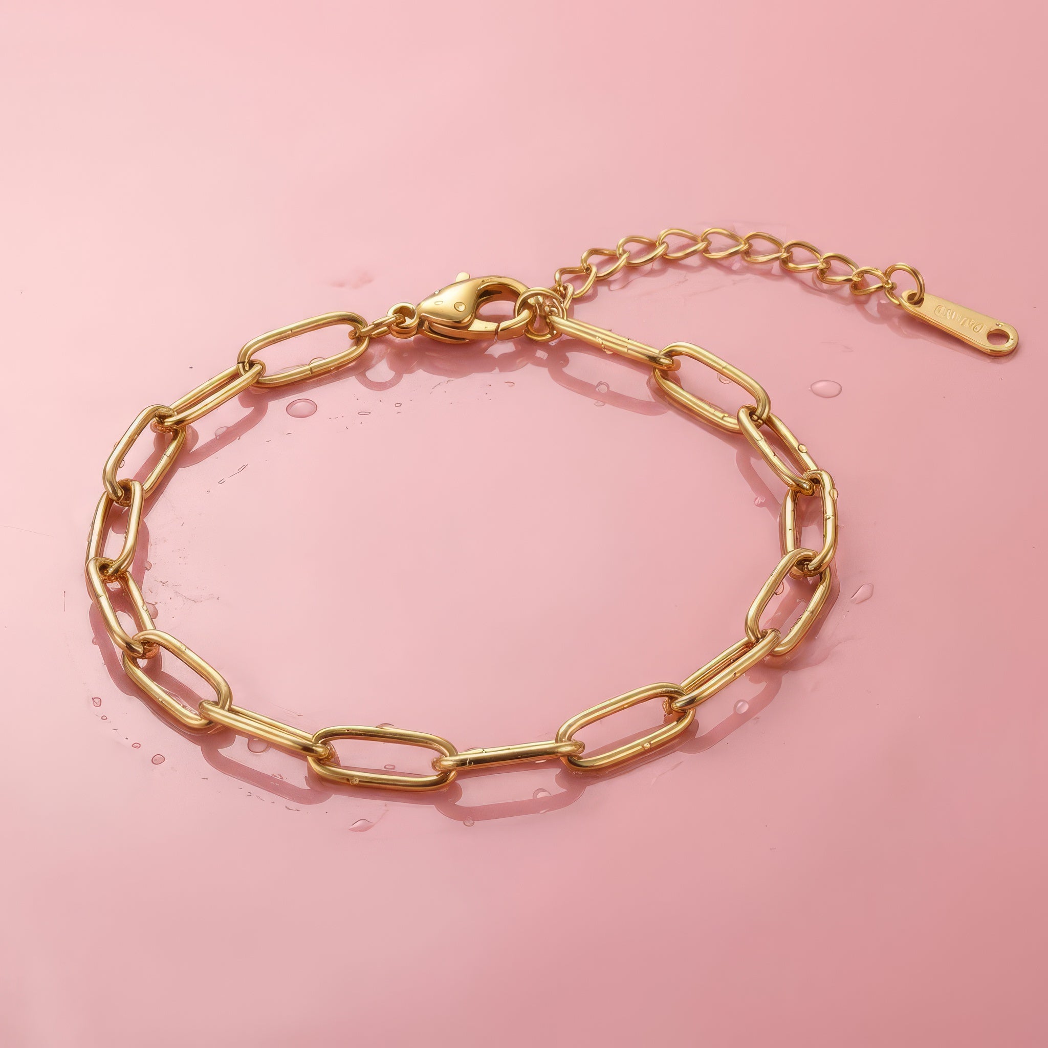 Gold paperclip chain bracelet on a wet pink surface