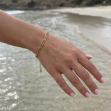 Gold paperclip chain bracelet on a woman's wrist above the ocean