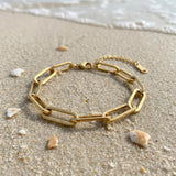 Gold paperclip chain bracelet lying on wet sand at the ocean