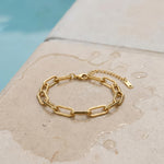 Gold paperclip chain bracelet lying on wet stone surface at the edge of the pool