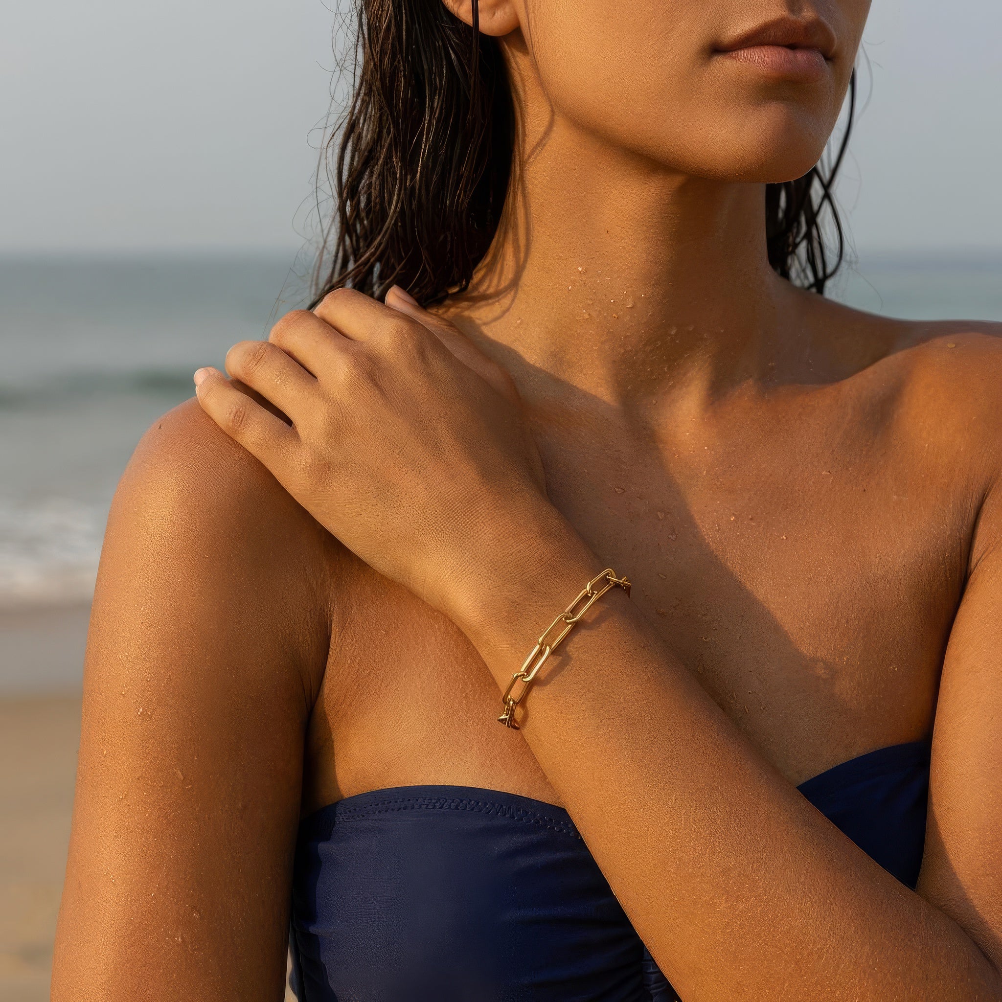 Woman wearing gold paperclip chain bracelet at the beach