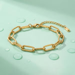 Gold paperclip chain bracelet on a wet mint green surface