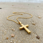 Gold cross necklace on a sandy beach