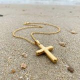 Gold cross necklace on a sandy beach
