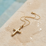 Gold cross necklace on a textured surface on the edge of a pool.
