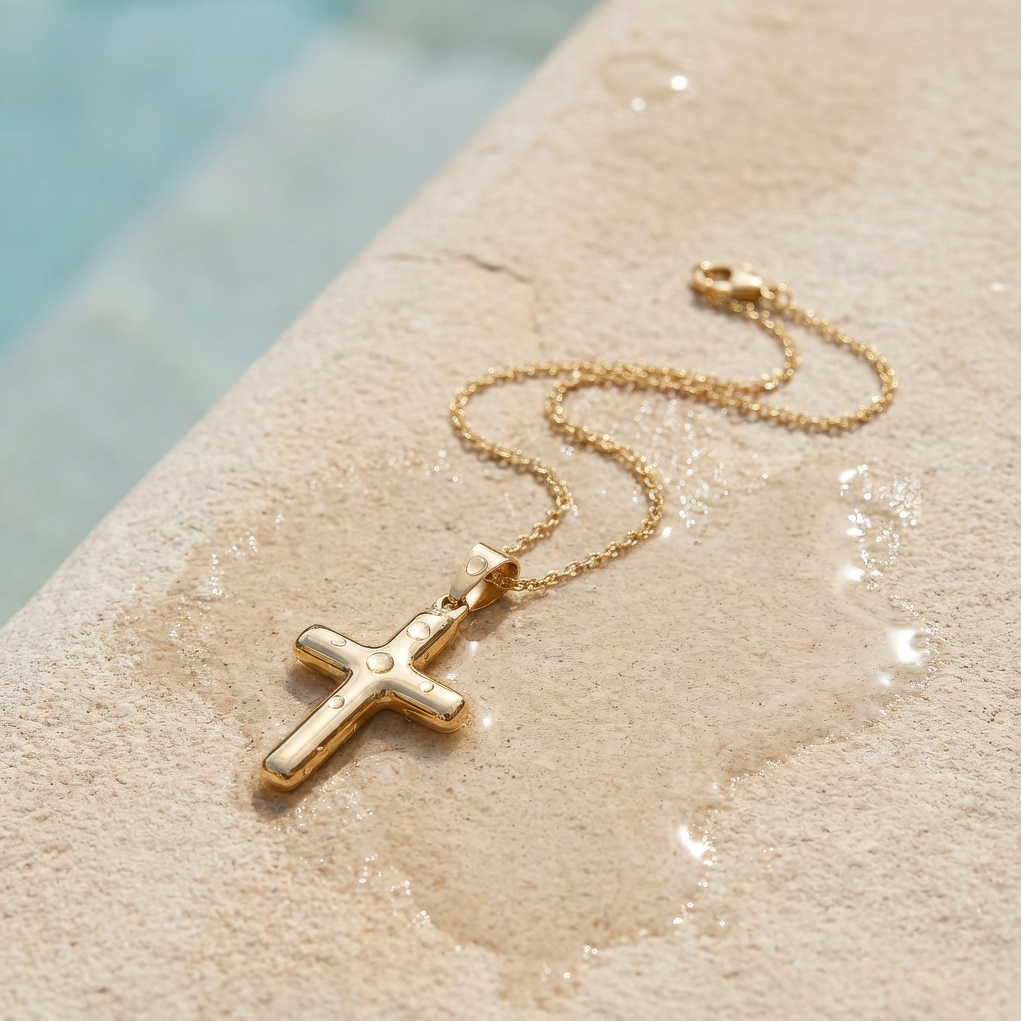 Gold cross necklace on a textured surface on the edge of a pool.