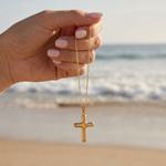 Hand holding gold cross necklace in front of the ocean.