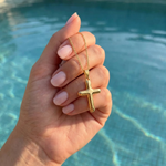 Gold cross necklace held in hand above pool water.