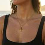 Woman wearing a gold cross necklace withat the beach.