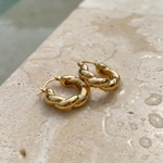 Gold hoop earrings on a textured stone surface at the edge of a pool