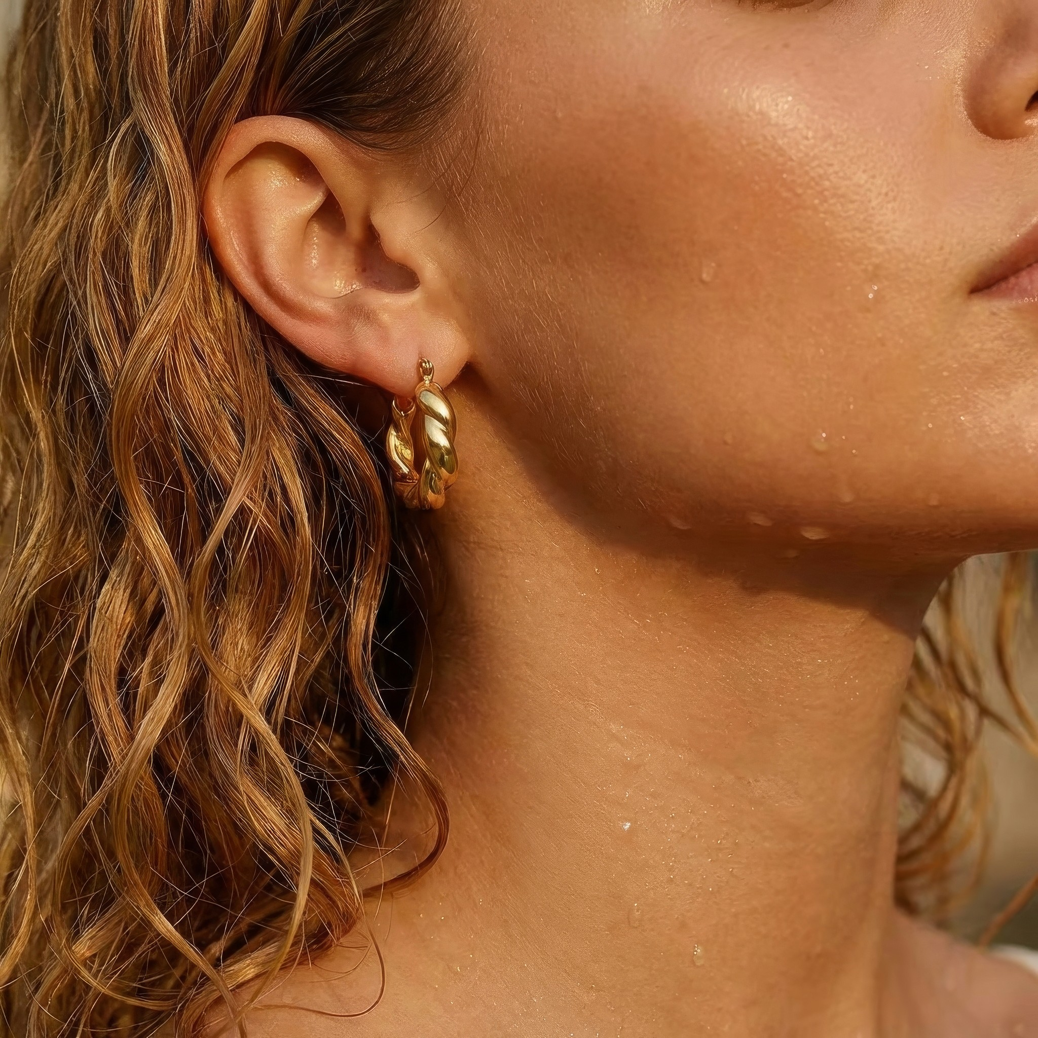 Close-up of a woman wearing gold hoop earrings with a blurred background