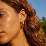 Close-up of a woman wearing gold hoop earrings with a blurred natural background