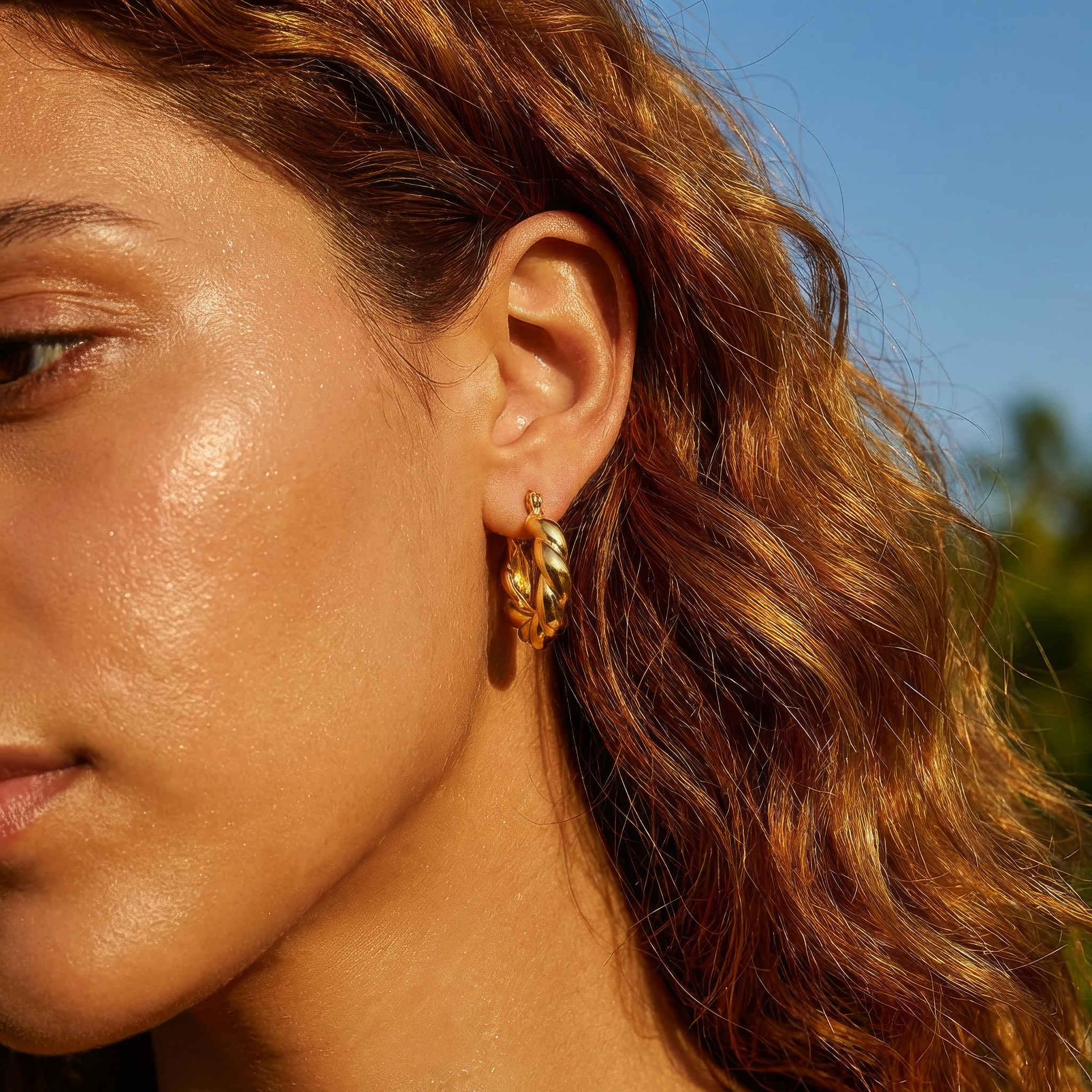 Close-up of a woman wearing gold hoop earrings with a blurred natural background