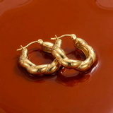 Gold hoop earrings on a wet reflective dark orange surface