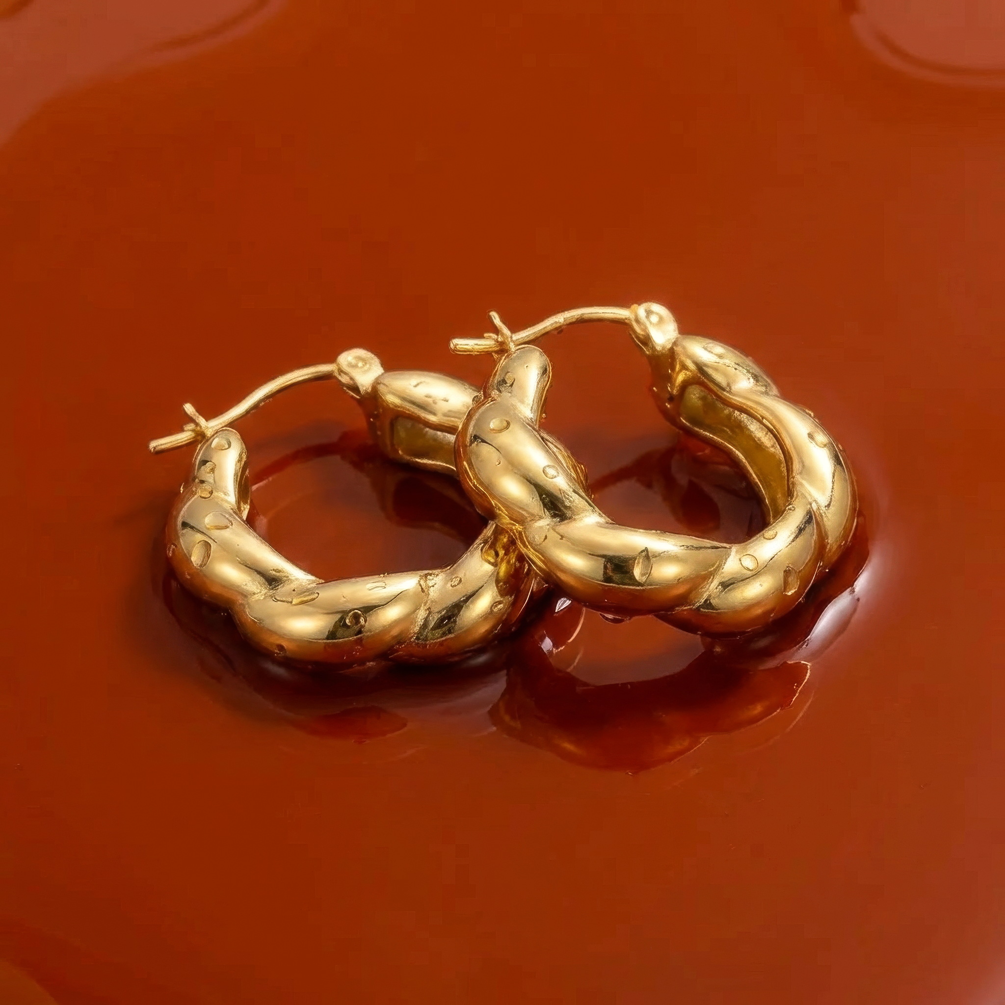Gold hoop earrings on a wet reflective dark orange surface
